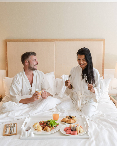 pár reggelizik az ágyban, férfiak és nők a hálószobában reggeliznek reggel. kávéval és gyümölcsökkel - Fotó, kép