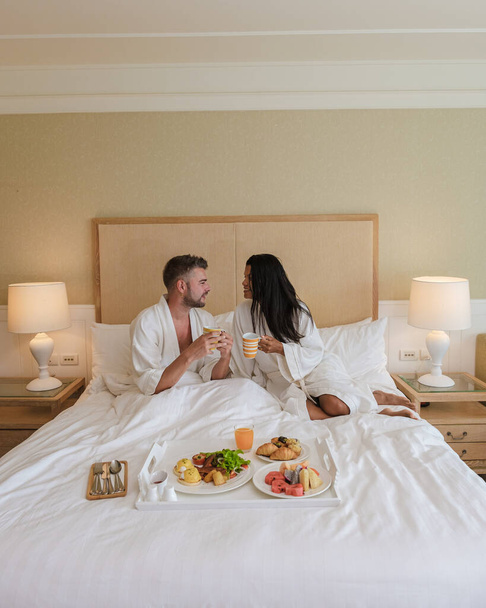 pareja desayunando en la cama, hombres y mujeres en el dormitorio desayunando por la mañana. con café y fruta - Foto, imagen