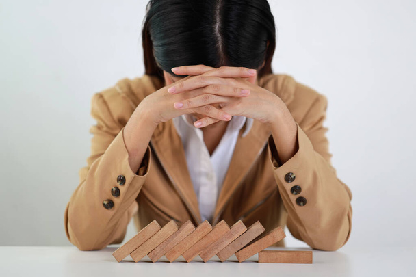 Businesswoman in classic suite touching her head and sitting, lying face down on table after wooden block dominoes falling. Investment Insurance or business risk control concept - Photo, Image