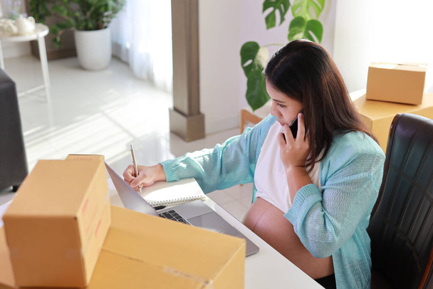 Attractive happy asian pregnant woman sitting and using mobile smart phone and writing order for customer with tablet. Expectant mother preparing and working for baby birth during pregnancy concept - Foto, afbeelding