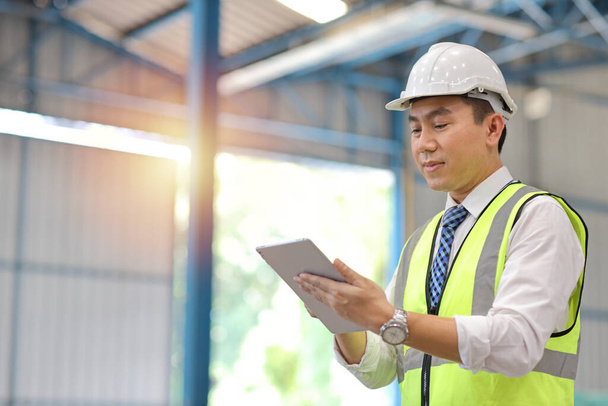 Architect or engineering man and worker standing and checking large warehouse with tablet. Asian business manager looking in future with warehouse building background. - Fotó, kép