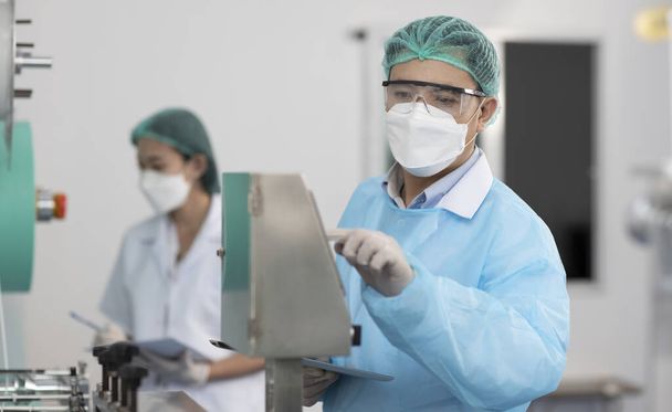 Inspektor mężczyzna i kolega kobieta pracuje nad jakością maski i maski medycznej linii produkcyjnej, Przemysł i koncepcja fabryki. - Zdjęcie, obraz