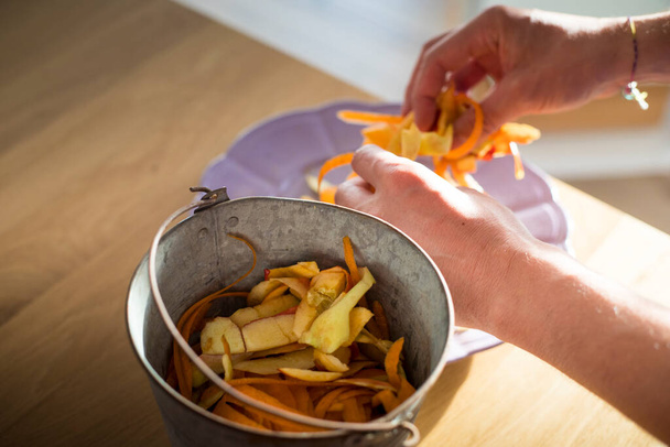 Male hands sorting vegetable peelings in tin bin. Use of food waste, composting, in order to enrich soil fertility. Garbage sorting at home. - Photo, Image
