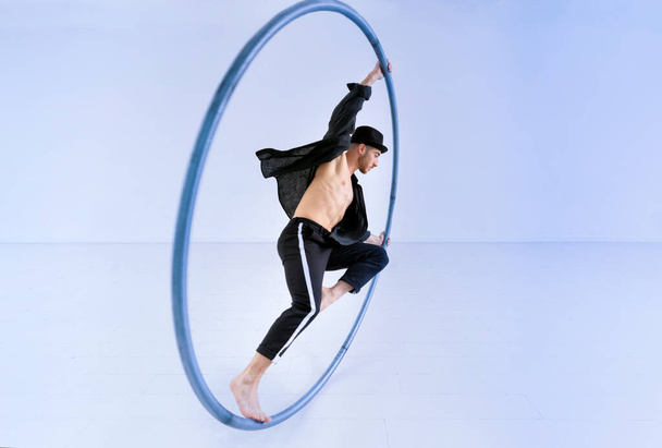 Ganzkörper-Barfuß-Mann im Kostüm macht Trick auf Cyr-Rad vor blauem Hintergrund bei akrobatischer Performance - Foto, Bild