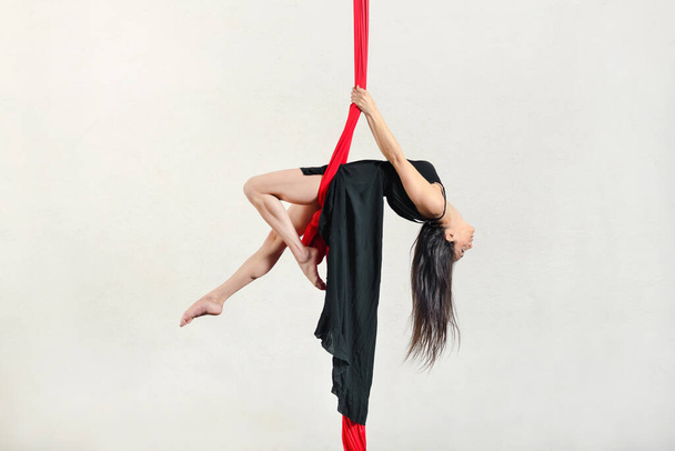 Full body side view of active female aerialist performing swing exercise on aerial silks against white background during training in studio - Photo, Image