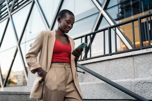 Vágott oldalán nézet egy afro-amerikai fiatal felnőtt nő rövid haj sétál le a lépcsőn a telefon a városban - Fotó, kép