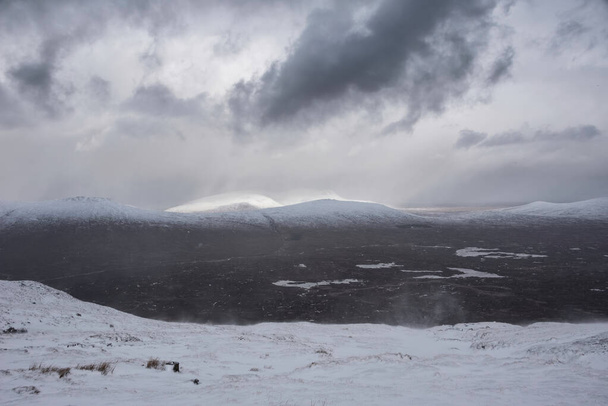 Beautiful Winter landscape image from mountain top in Scottish Highlands down towards Rannoch Moor during snow storm and spindrift off mountain top in high winds - Photo, Image