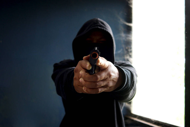 Злочинця в чорному капюшоні, який тримає вогнепальну зброю, грабіжника Маска з пістолетом на руках, щоб скоїти злочин у покинутому будинку. - Фото, зображення