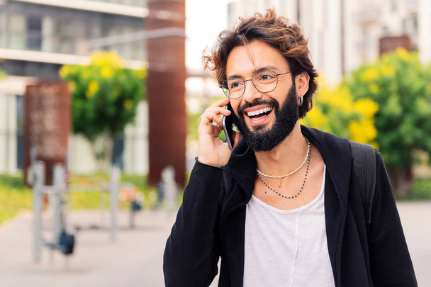 stylish young man with smiling happy while talking on mobile phone in the city, concept of urban lifestyle and technology of communication, copy space for text - Photo, Image