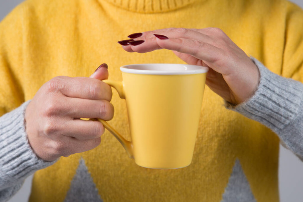 Női kéz tart egy sárga csésze forró ital, a háttérben egy sárga pulóver, koncepció, szelektív fókusz - Fotó, kép