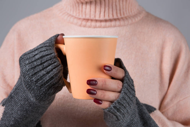 En manos femeninas con mangas largas de un suéter de lana una taza con una bebida caliente, el concepto de calidez y comodidad, enfoque selectivo - Foto, Imagen