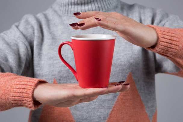 In female hands there is a red cup with a hot drink, one hand is above the cup, the concept of warmth in the cold season, selective focus - Fotó, kép