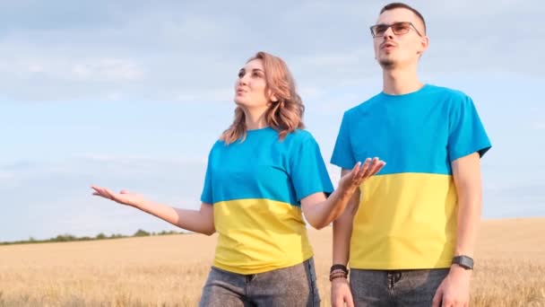 Ukrajinská rodina je oblečena v šatech vlajky, v modrých a žlutých barvách. Muž a žena zpívají uprostřed pšeničného pole. Koncept války na Ukrajině - Záběry, video