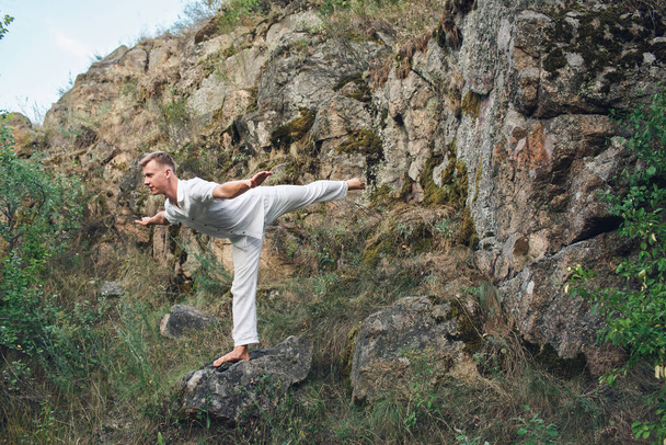 een jonge kerel doet yoga in de buurt van een rots - Foto, afbeelding
