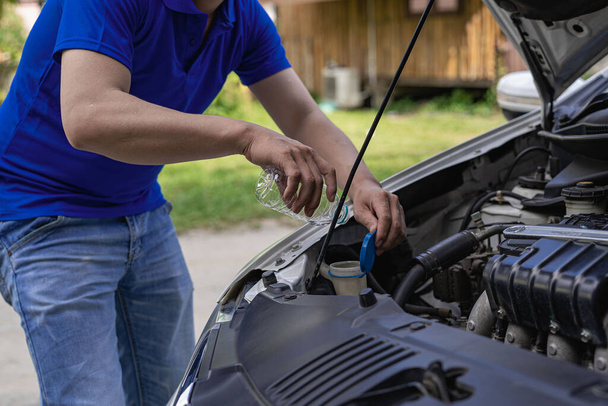 Een jongeman controleert het oliepeil en repareert de auto voordat hij vertrekt.. - Foto, afbeelding