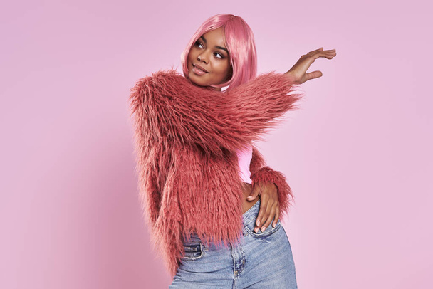 Attractive young African woman with pink hair standing against pink background - Fotó, kép