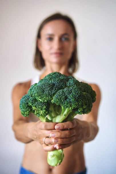 young woman dressed in white t-shirt showing with broccoli. High quality photo - Foto, Bild