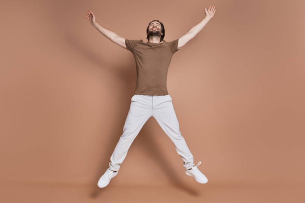 Full length of happy young man jumping against brown background - Фото, изображение
