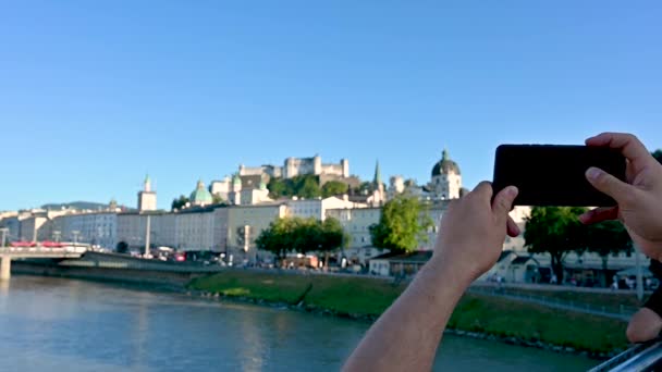 Salzburg, Oostenrijk, augustus 2022. Mooie slow motion beelden overdag met voorgrondbeeld op een mobiele telefoon in de handen om foto 's te maken, op de achtergrond de oude stad gedomineerd door het fort - Video