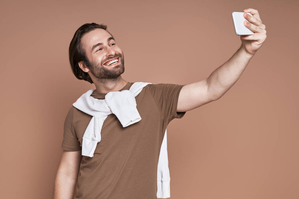 Boldog fiatalember, hogy szelfi okos telefon a barna háttér - Fotó, kép