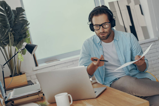 Handsome young man in headphones discussing business during web conference in office - Фото, изображение
