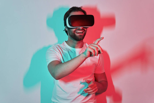 Confident young man in virtual reality eyeglasses gesturing with colorful shadows in the background - Fotografie, Obrázek