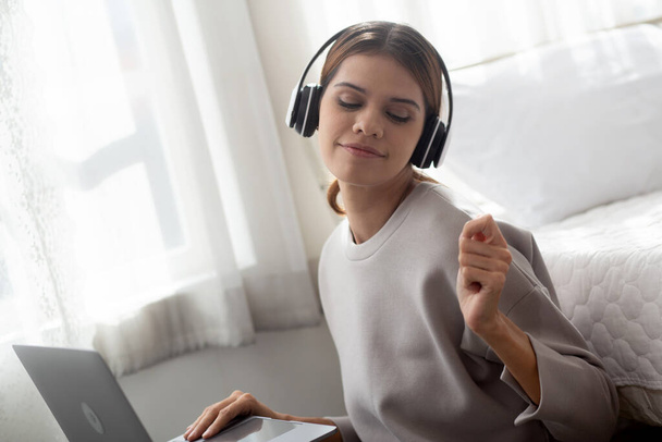 Happy young woman wearing headphones listening music while using laptop computer and singing with fun and enjoy in the living room, happiness female with entertainment, lifestyles concept. - Foto, afbeelding