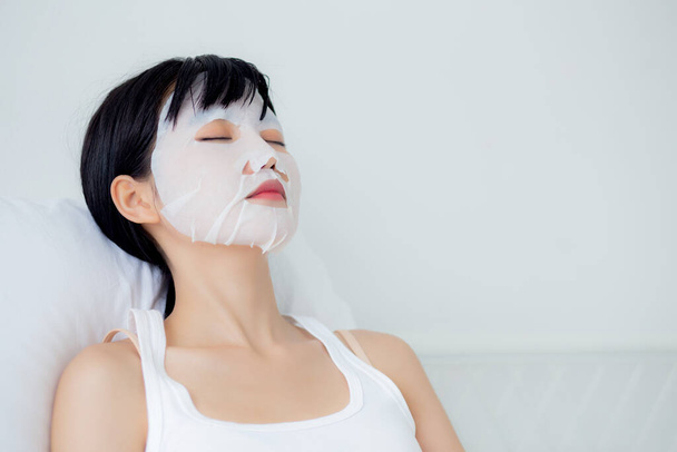 Piękna młoda azjatycka kobieta z prześcieradłem maski twarzy i snu na łóżku w sypialni, piękna dziewczyna stosująca kosmetyki i makijaż z twarzy do pielęgnacji skóry na zmarszczki, leczenie skóry, zdrowie i wellness. - Zdjęcie, obraz