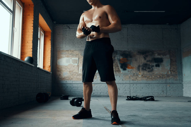 Unrecognizable muscular man wearing sport gloves while standing in gym - Foto, imagen