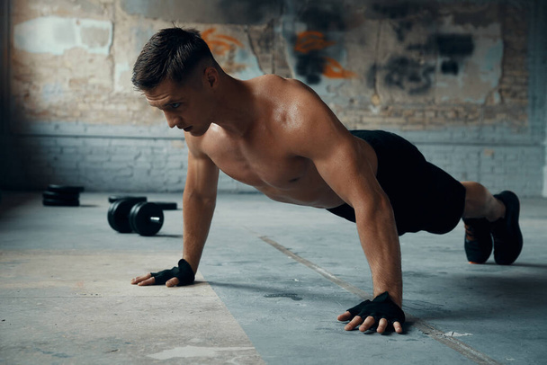 Confident young man doing push-up exercises in gym - 写真・画像