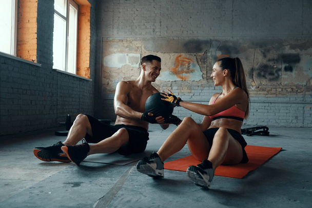 Happy fit couple exercising with medicine ball while sitting on exercise mats in gym - Fotografie, Obrázek