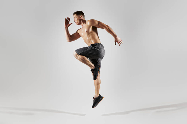 Confident muscular man with perfect body jumping against white background - Valokuva, kuva