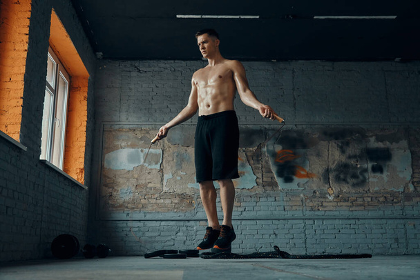 Full length of handsome young man jumping with rope while exercising in gym - Foto, afbeelding