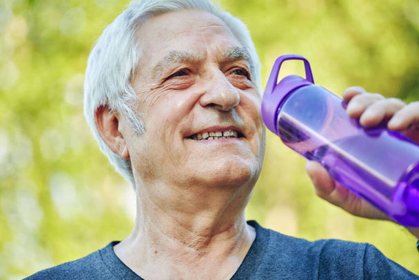 Close up image attractive mature man holds plastic reusable bottle drinking still mineral water during morning work out or stroll in summer park, caring about health, relieving thirst - Foto, Imagem