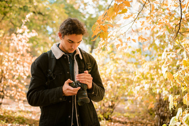 Krajobraz i fotograf przyrody patrząc przez swoje zdjęcia przed kamerą, stojąc w lesie pomiędzy żółtymi, czerwonymi jesiennymi drzewami - Zdjęcie, obraz