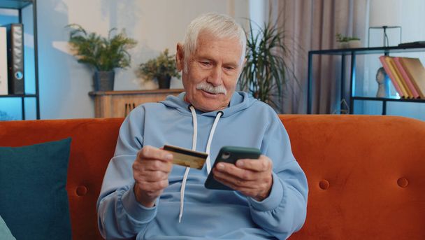 Щасливий шопоголічний споживач старший старий дід, що сидить вдома, робить онлайн замовлення доставки їжі, оплату кредитною пластиковою банківською карткою. Продаж знижок в Інтернеті. Літній пенсіонер
 - Фото, зображення