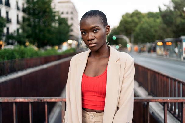 Portrait of an african american young woman with short hair standing and looking at camera on a footbridge in the city - Foto, imagen