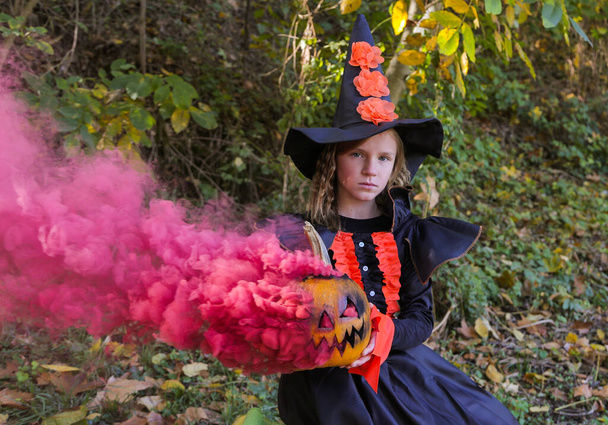 Κορίτσι ντυμένος ως μάγισσα για Απόκριες με κολοκύθα σε μαγικό καπνό στο δάσος . - Φωτογραφία, εικόνα