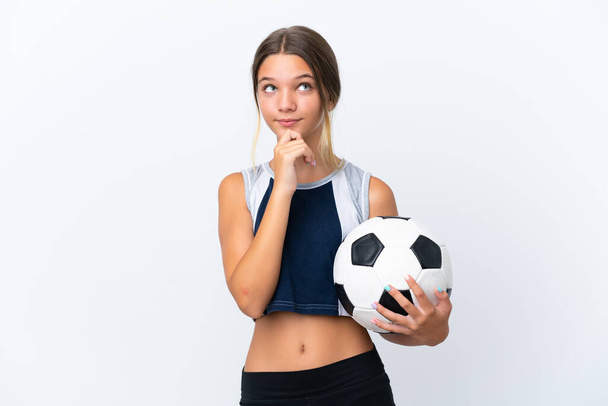 Маленькая кавказская девочка играет в футбол на белом фоне и смотрит вверх - Фото, изображение