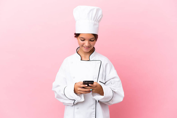 Little kaukaski szef kuchni dziewczyna odizolowany na różowym tle wysyłanie wiadomości z telefonu - Zdjęcie, obraz