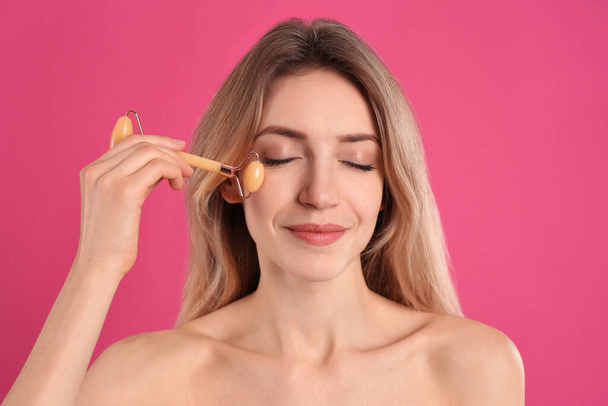 Young woman using natural jade face roller on pink background - Foto, immagini