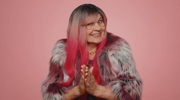 Sneaky cunning woman with tricky face gesticulating and scheming evil plan, thinking over devious villain idea, cunning cheats, jokes and pranks. Senior grandmother on pink studio background indoors - Photo, Image
