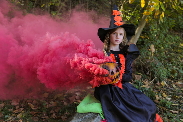Dziewczyna ubrana jak czarownica na Halloween z dyni w magicznym dymem w lesie . - Zdjęcie, obraz