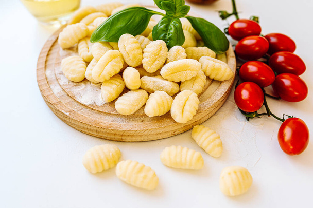 Austrian cuisine gnocchi. Potato and flour dumplings, on wooden round board, served with basil and tomato sauce. Ingredients for gnocchi including fresh gnocchi, tomatoes, olive oil, potatoes - Photo, Image