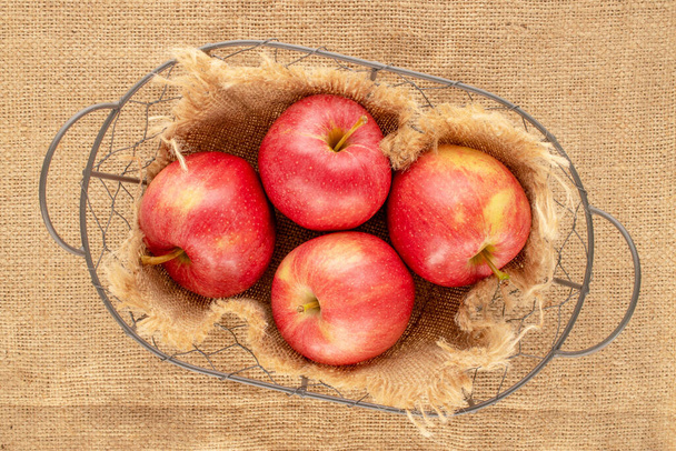Несколько сладких красных яблок в корзине на джут ткани, макрос, вид сверху. - Фото, изображение