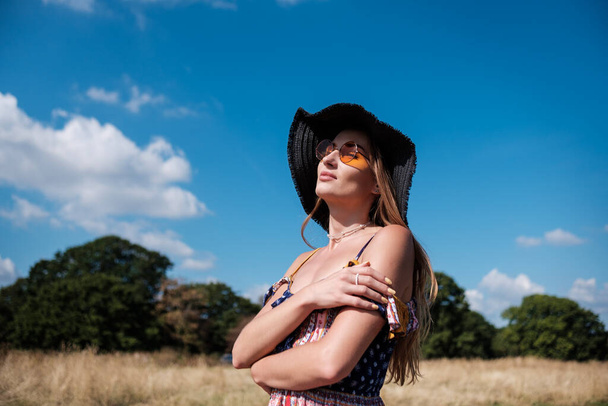 Portrait of young caucasian woman wearing sunglasses, straw hat and summer dress. She is in a field in a summer sunny day. - Foto, immagini