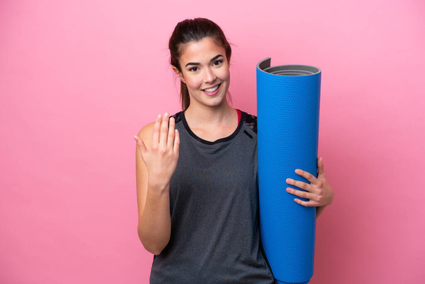 Young Brazilian sport woman going to yoga classes while holding a mat isolated on pink background inviting to come with hand. Happy that you came - Foto, Imagem