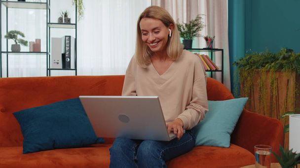 Portrait of caucasian girl sitting on couch, looking at camera, making video webcam conference call with friends or family, enjoying pleasant conversation. Young woman laughing, waving hello at home - Photo, Image
