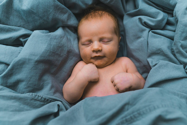Nahaufnahme Porträt eines entzückenden kleinen Jungen, der auf einem Bett liegt, das mit dunkelblauen Bettwäsche bedeckt ist. Neues Leben. Hochwertiges Foto - Foto, Bild