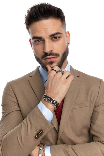 portrét zamyšleného mladého podnikatele držícího ruku na bradě a přemýšlejícího při pózování na bílém pozadí ve studiu - Fotografie, Obrázek